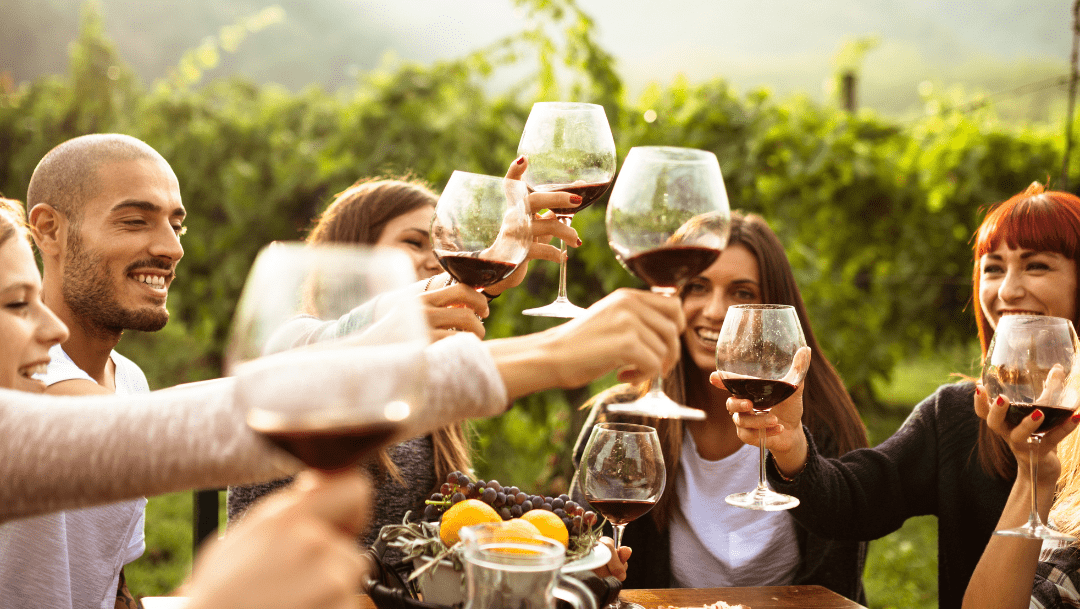 People toasting with glasses of wine. There is foliage in the background behind them